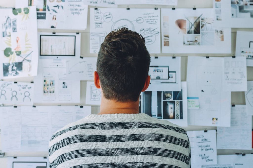 man-wearing-black-and-white-stripe-shirt-looking-at-white-printer-papers-on-the-wall-212286 A man stands in front of a wall filled with creative ideas and plans. Ideal for innovation themes.
